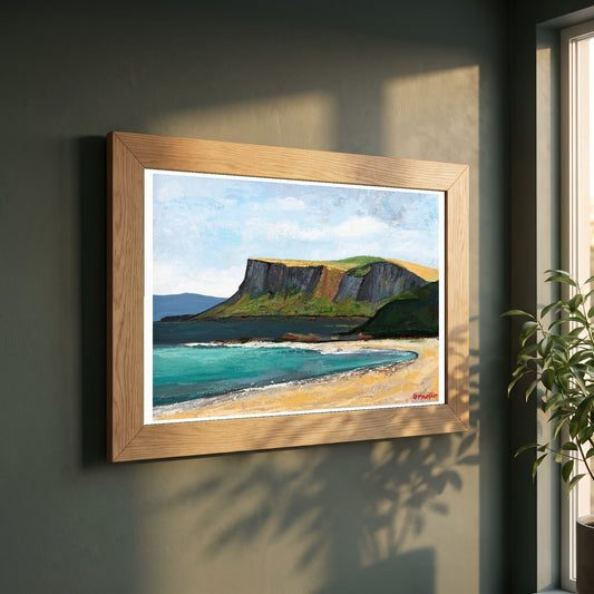 Fair Head from Ballycastle Beach framed print in a natural oak frame on a dark green wall beside a window, dappled plant shadow