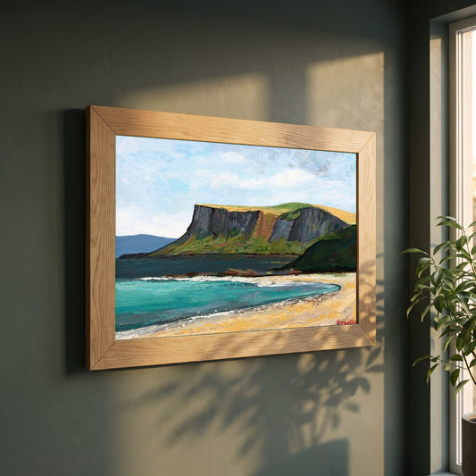 Fair Head from Ballycastle Beach framed print in a natural oak frame on a dark green wall beside a window, dappled plant shadow
