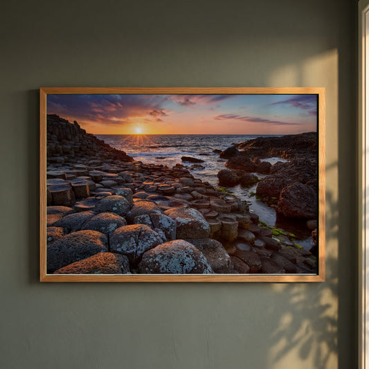 Giant's Causeway framed print in a natural oak frame on a dark green wall beside a window, dappled plant shadow