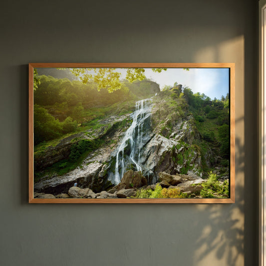 Powerscourt Waterfall Wicklow framed print in a natural oak frame on a dark green wall beside a window, dappled plant shadow