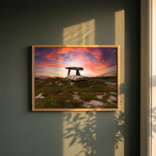 Poulnabrone Dolmen framed print in a natural oak frame on a dark green wall beside a window, dappled plant shadow