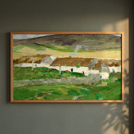 The White Cottage framed print in a natural oak frame on a dark green wall beside a window, dappled plant shadow