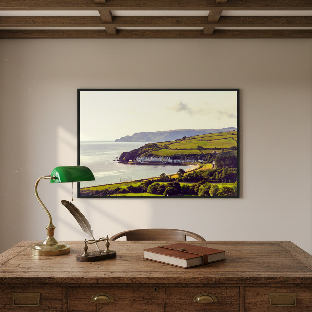 Cushendun print in black frame above a vintage writing desk with brass lamp, exposed beams and sea views through a sash window.