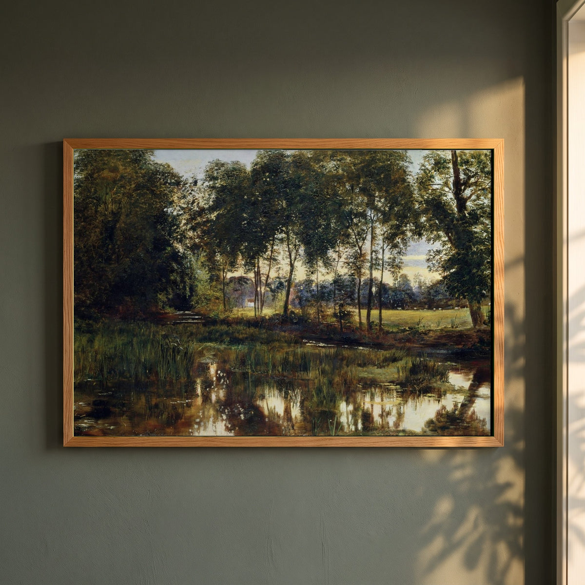 A View of Rye Water near Leixlip framed print in a natural oak frame on a dark green wall beside a window, dappled plant shadow