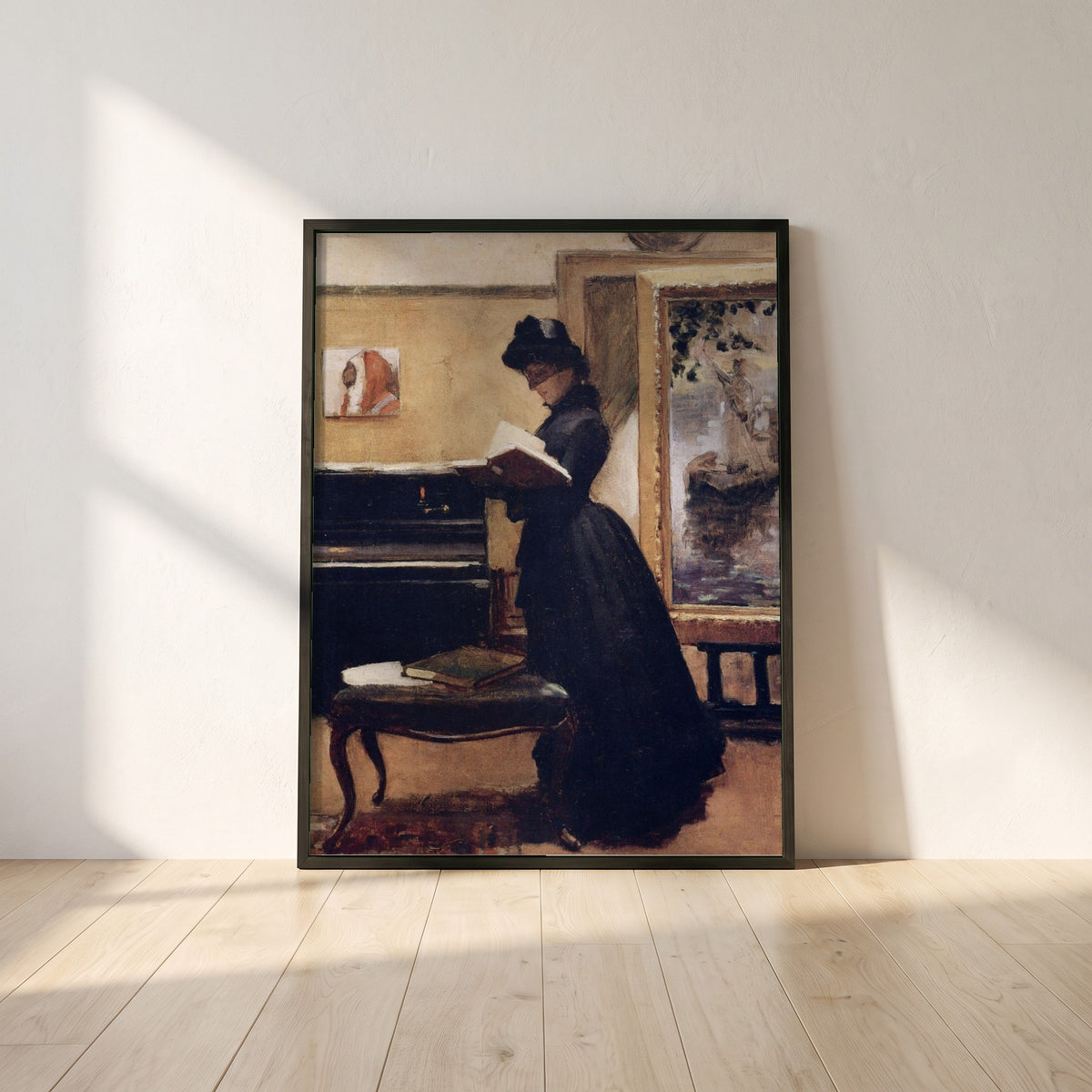 A Visit to the Studio framed print in a black frame leaning against a white plaster wall on oak floorboards in morning light