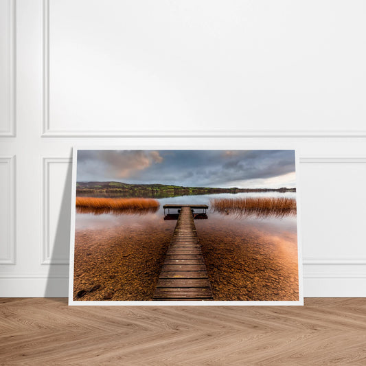 Old Jetty, Lough Derg photographic print, wooden jetty through golden reeds, white frame leaning on a panelled wall