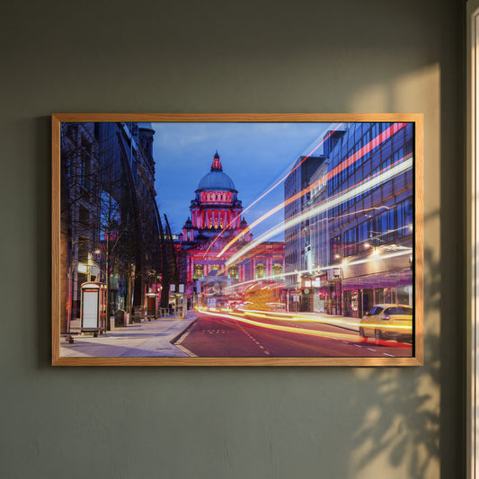 Belfast City Photography framed print in a natural oak frame on a dark green wall beside a window, dappled plant shadow
