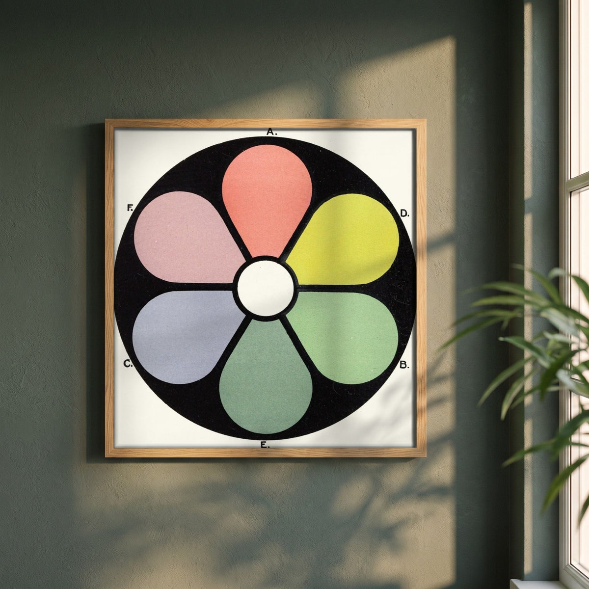 Broken Tones of the Primaries by James Ward framed print in a natural oak frame on a dark green wall beside a window, dappled plant shadow