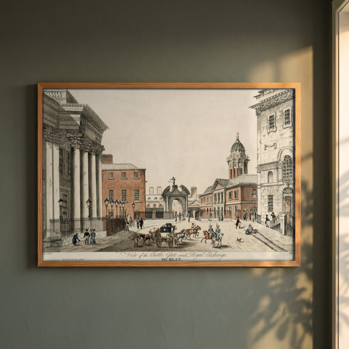 Dublin Castle Gate framed print in a natural oak frame on a dark green wall beside a window, dappled plant shadow