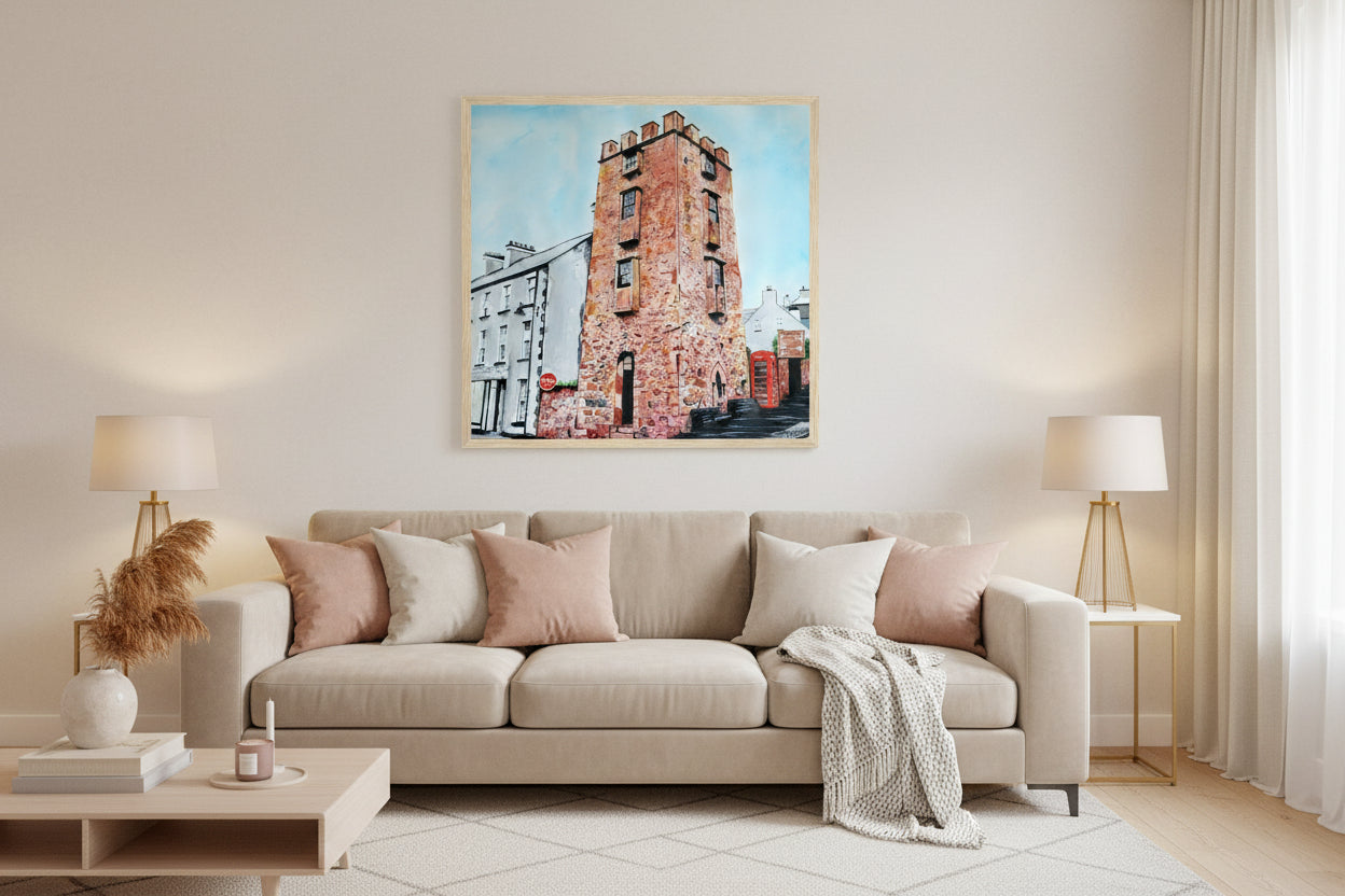 Stylish modern living room with soft neutrals, subtle feminine décor, plush textures, warm lamp lighting, framed Cushendall Curfew Tower print as focal point. Framed art print 'The Curfew Tower' by Ó Maoláin. This piece depicts The Curfew Tower in Cushendall, Glens of Antrim, built by Francis Turnley in 1820 and now owned by Bill Drummond. The artwork showcases the tower amid the scenic Glens of Antrim. Buy Irish Art