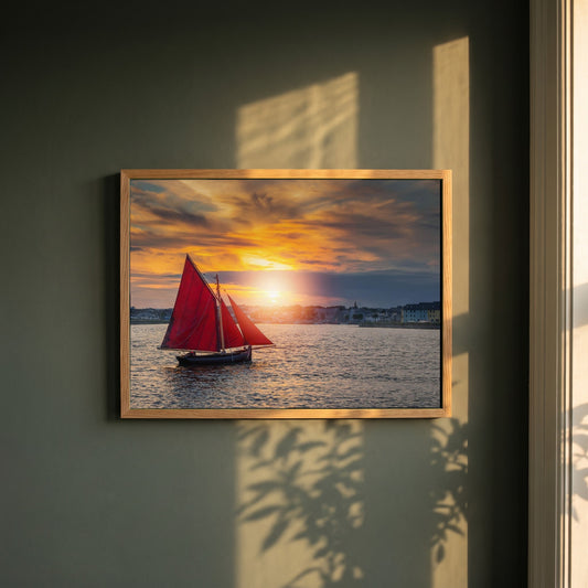 Galway Hooker framed print in a natural oak frame on a dark green wall beside a window, dappled plant shadow