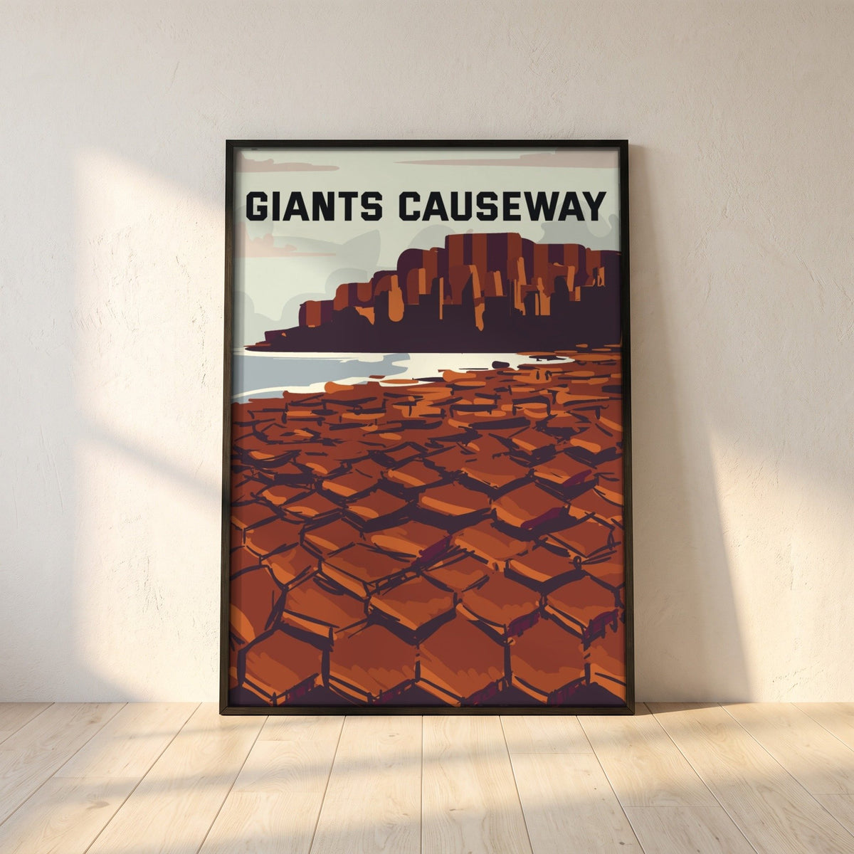 Giant's Causeway retro travel poster in a black frame leaning against a white plaster wall on oak floorboards in morning light
