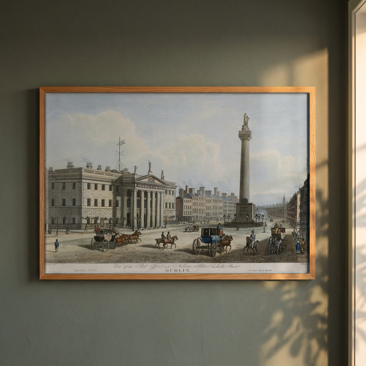 GPO & Nelson's Pillar, Dublin framed print in a natural oak frame on a dark green wall beside a window, dappled plant shadow