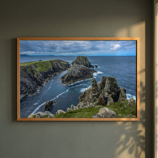 Inishowen Peninsula framed print in a natural oak frame on a dark green wall beside a window, dappled plant shadow