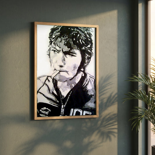 Joey Dunlop framed print in a natural oak frame on a dark green wall beside a window, dappled plant shadow