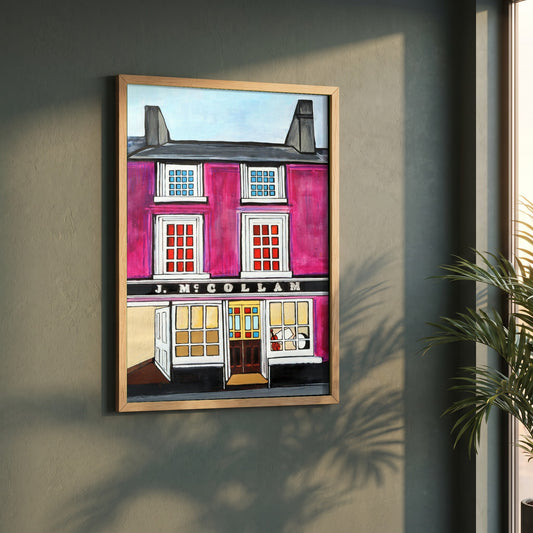 Johnny Joe's Pub, Cushendall framed print in a natural oak frame on a dark green wall beside a window, dappled plant shadow
