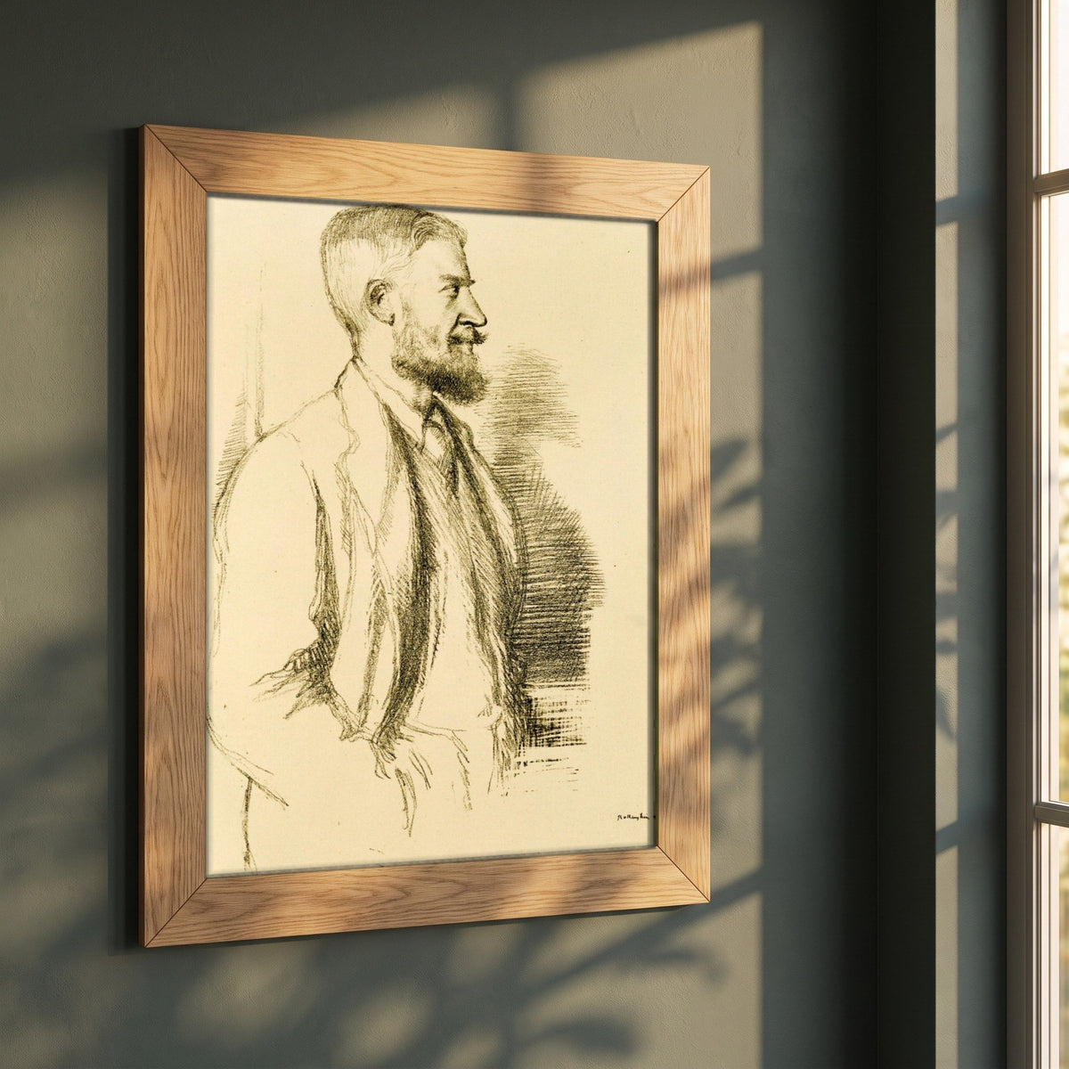 Mr George Bernard Shaw (1897) by William Rothenstein framed print in a natural oak frame on a dark green wall beside a window, dappled plant shadow