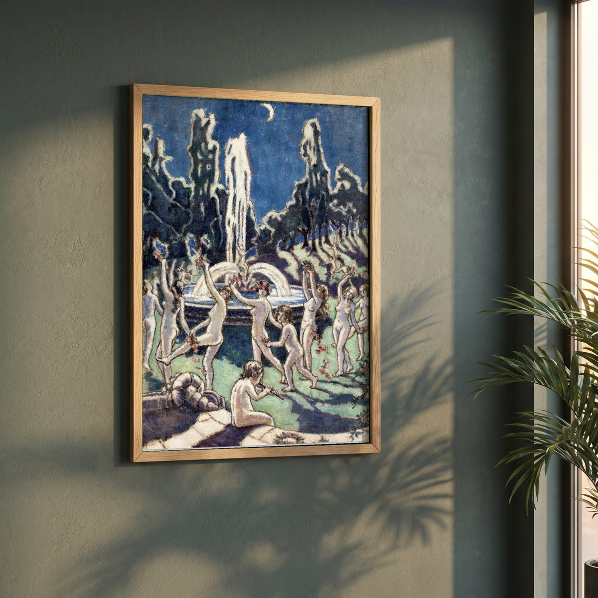 Figures Dancing Round a Fountain framed print in a natural oak frame on a dark green wall beside a window, dappled plant shadow