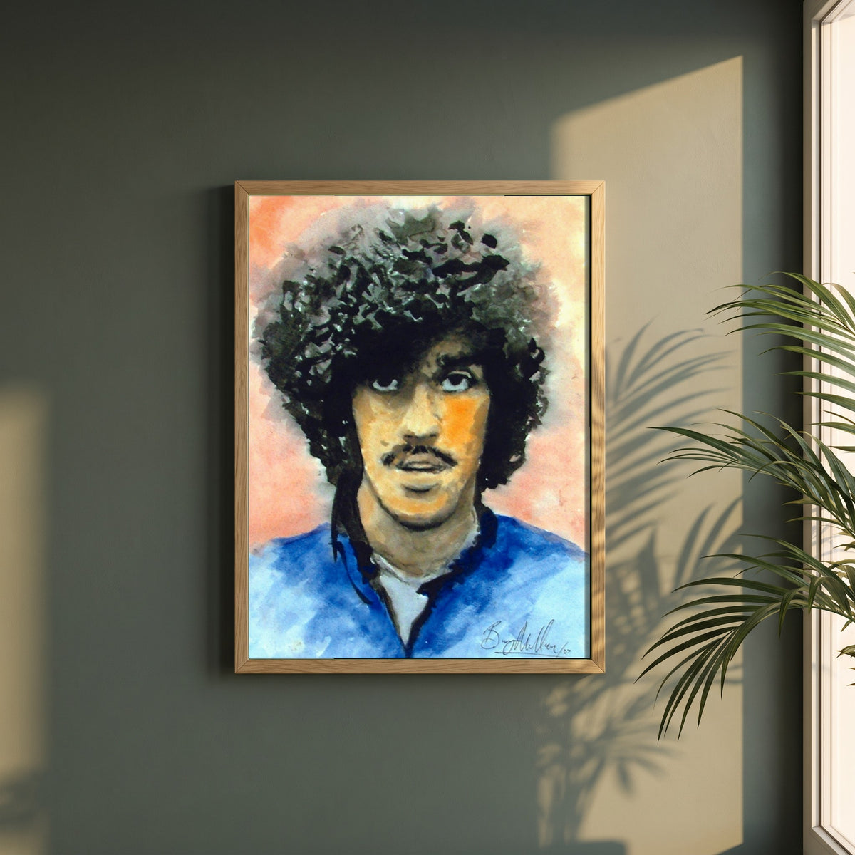 Phil Lynott Thin Lizzy framed print in a natural oak frame on a dark green wall beside a window, dappled plant shadow