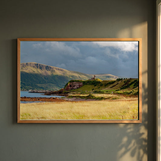 Red Bay Castle framed print in a natural oak frame on a dark green wall beside a window, dappled plant shadow