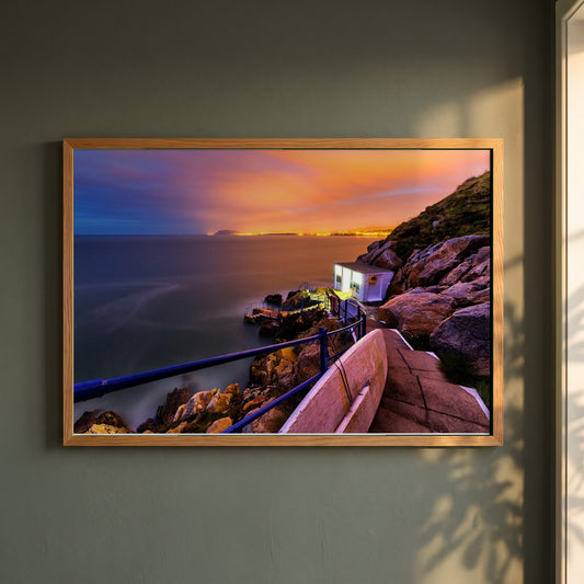 Sunrise in Hawk Cliff Killiney, Co. Dublin, Ireland framed print in a natural oak frame on a dark green wall beside a window, dappled plant shadow