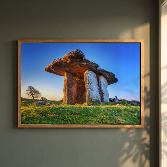 The Burren Poulnabrone Dolmen framed print in a natural oak frame on a dark green wall beside a window, dappled plant shadow