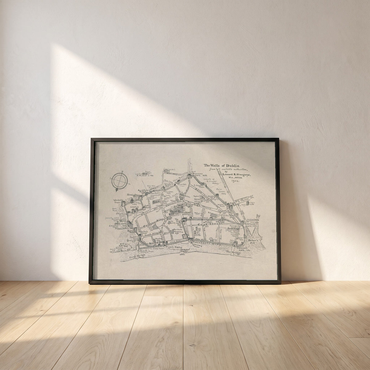 The Walls of Dublin framed print in a black frame leaning against a white plaster wall on oak floorboards in morning light