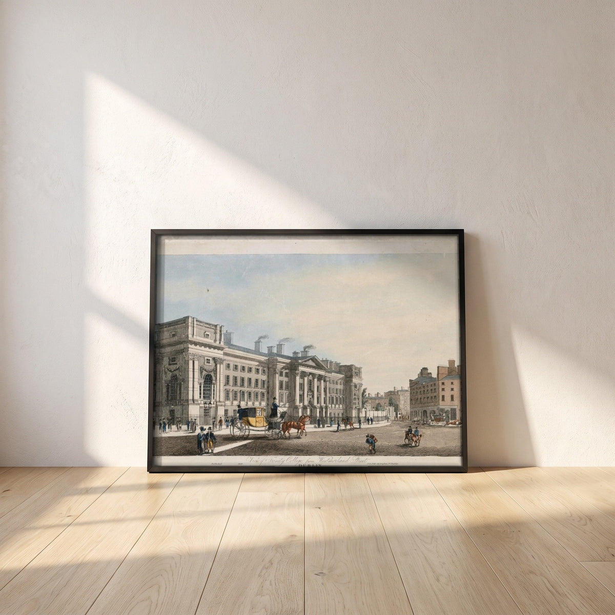Trinity College Dublin from Westmoreland Street framed print in a black frame leaning against a white plaster wall on oak floorboards in morning light